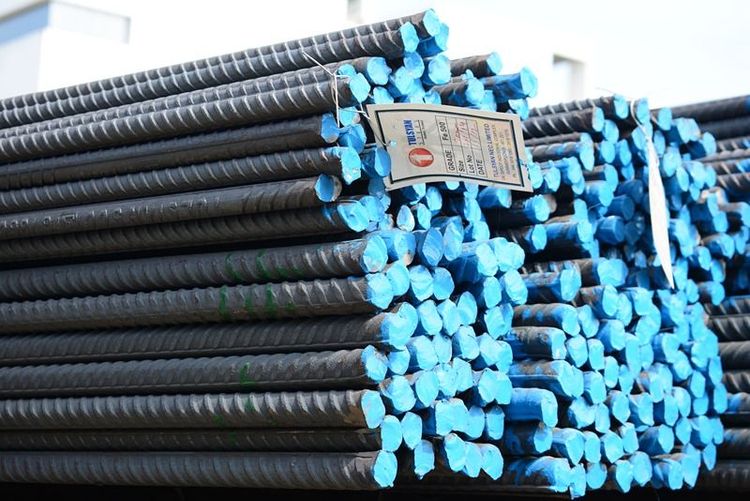 bundles_of_tmt_bars_in_a_factory_setting_with_workers_in_the_background