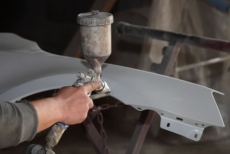 technician_using_spray_gun_to_apply_primer_on_car_body_panel