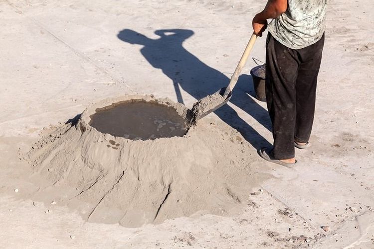 gloved_hand_holding_trowel_with_cement_powder_over_open_paper_bag