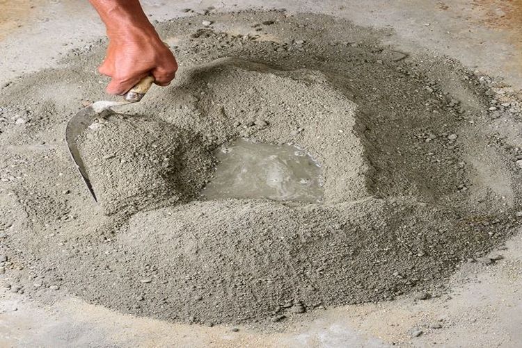 worker_mixing_dry_cement_powder_with_water_on_ground_using_trowel