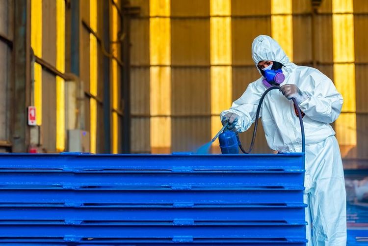 worker_in_industrial_clothing_spray_painting_steel_beams_blue_in_factory_setting