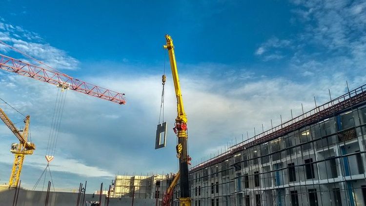 Yellow_crane_is_lifting_a_part_of_pre-cast_cement_wall_to_the_top_of_building_at_condominium_construction_site