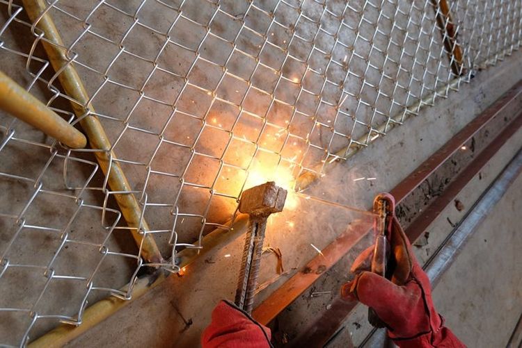Workers_wearing_leather_gloves_are_welding_a_steel_mesh_with_a_round_steel_tube_using_a_hammer_as_an_aid.