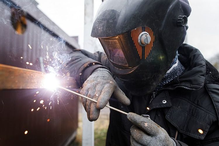 Shielded_metal_arc_welding._Worker_welding_metal_with_electrodes,_wearing_protective_helmet_and_gloves._Close_up_of_electrode_welding_and_electric_sparks
